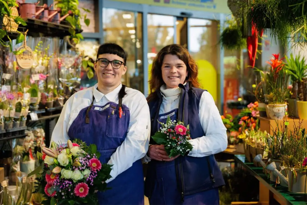 Zwei l&auml;chelnde Floristinnen im Blumenladen mit bunten Str&auml;u&szlig;en und Pflanzen &ndash; Floristik, Geschenkideen, Fr&uuml;hlingsblumen