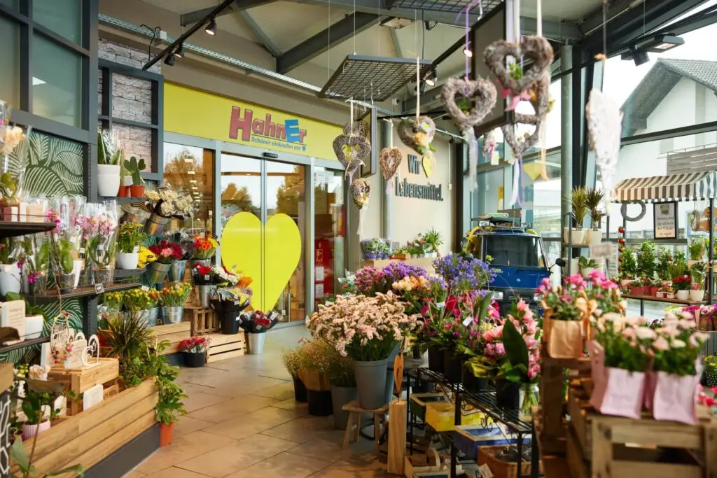 Blumenverkauf am Supermarkt-Eingang: frische Str&auml;u&szlig;e, Topfpflanzen und Herz-Dekorationen