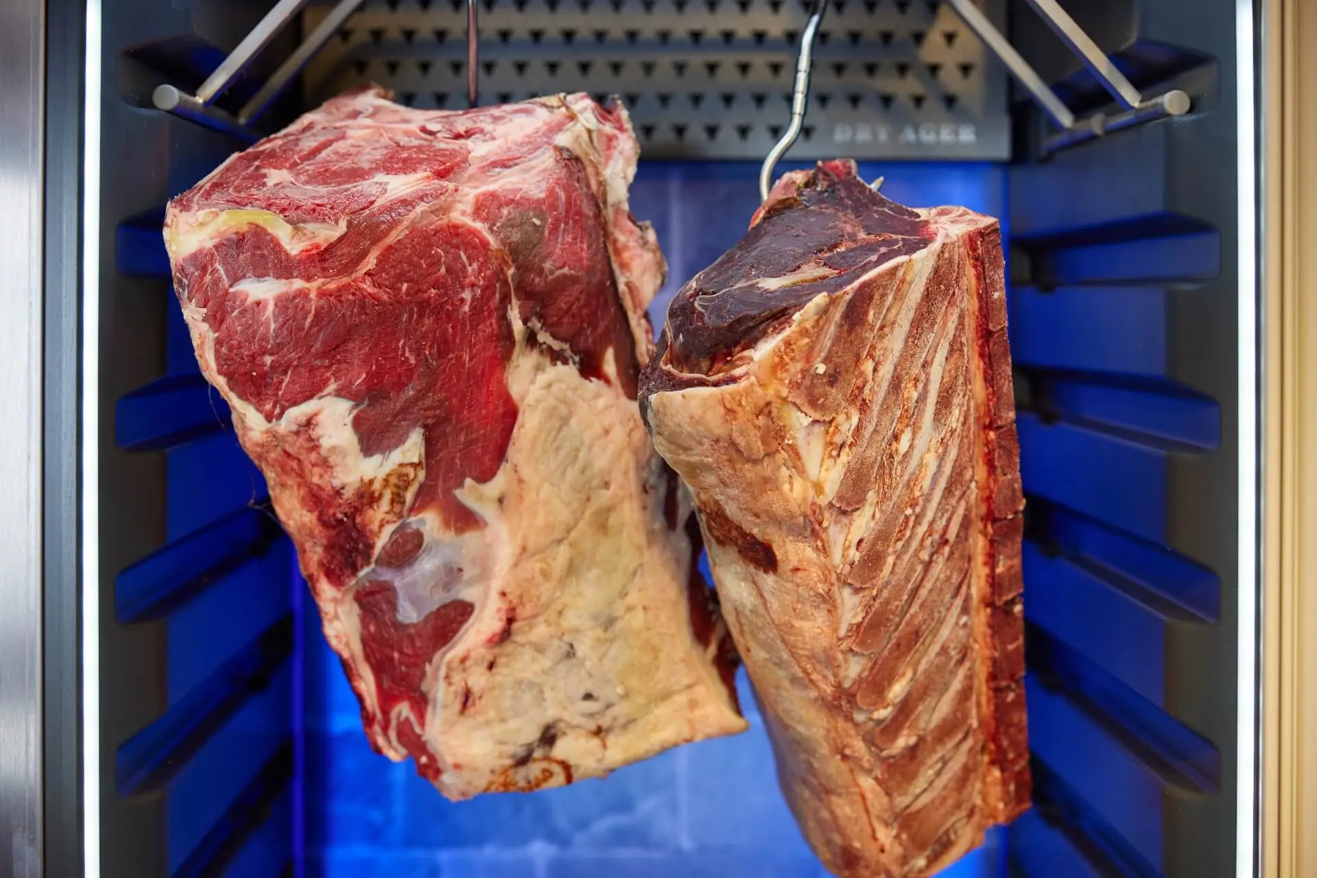 Dry-Aged Rindfleisch im Reifeschrank – zwei hängende Rinderrücken mit ausgeprägter Marmorierung und Trockenreifung