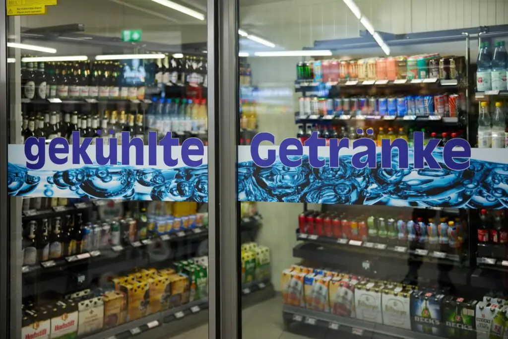 Glasfront mit Aufschrift gekühlte Getränke vor Supermarkt-Kühlschrank mit Bier, Wasser und Dosen