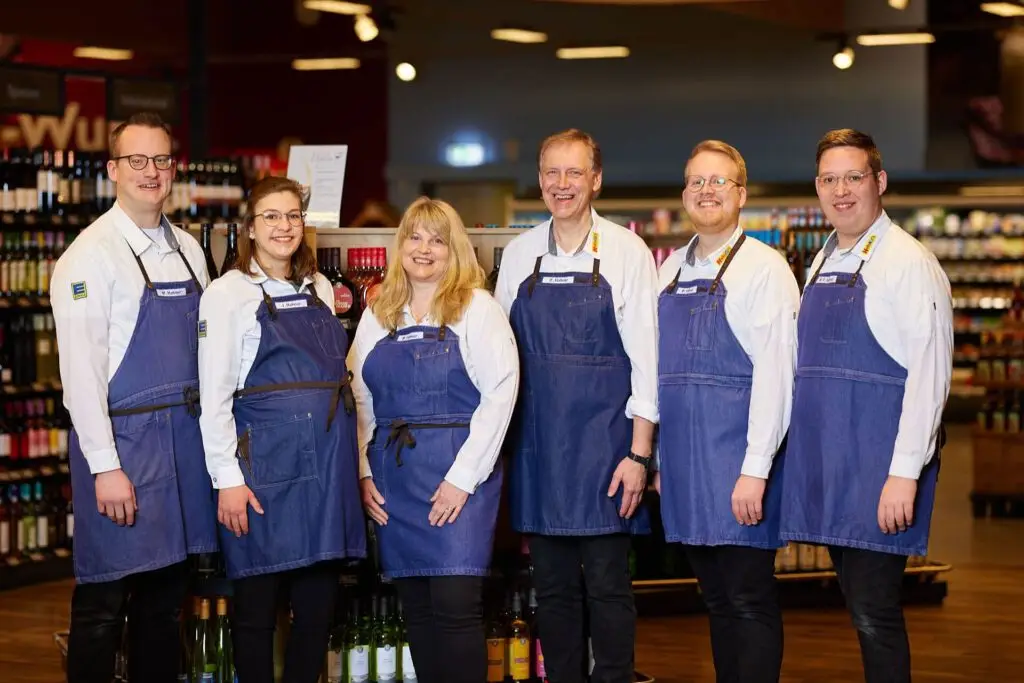 Supermarkt-Team in blauen Sch&uuml;rzen in der Weinabteilung, freundliche Beratung und Service