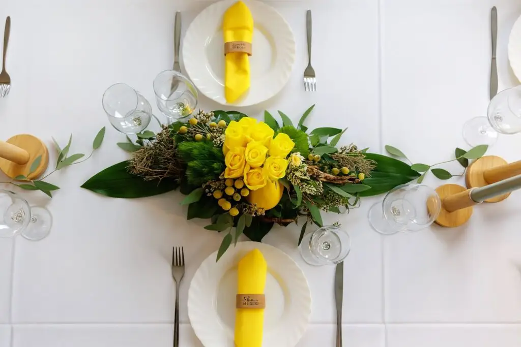 Tischdekoration mit gelben Rosen, gelben Servietten, wei&szlig;em Tischtuch, Gedeck mit Besteck und Weingl&auml;sern